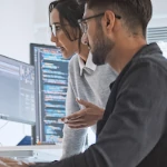 Two cybersecurity professionals looking at code on a computer.